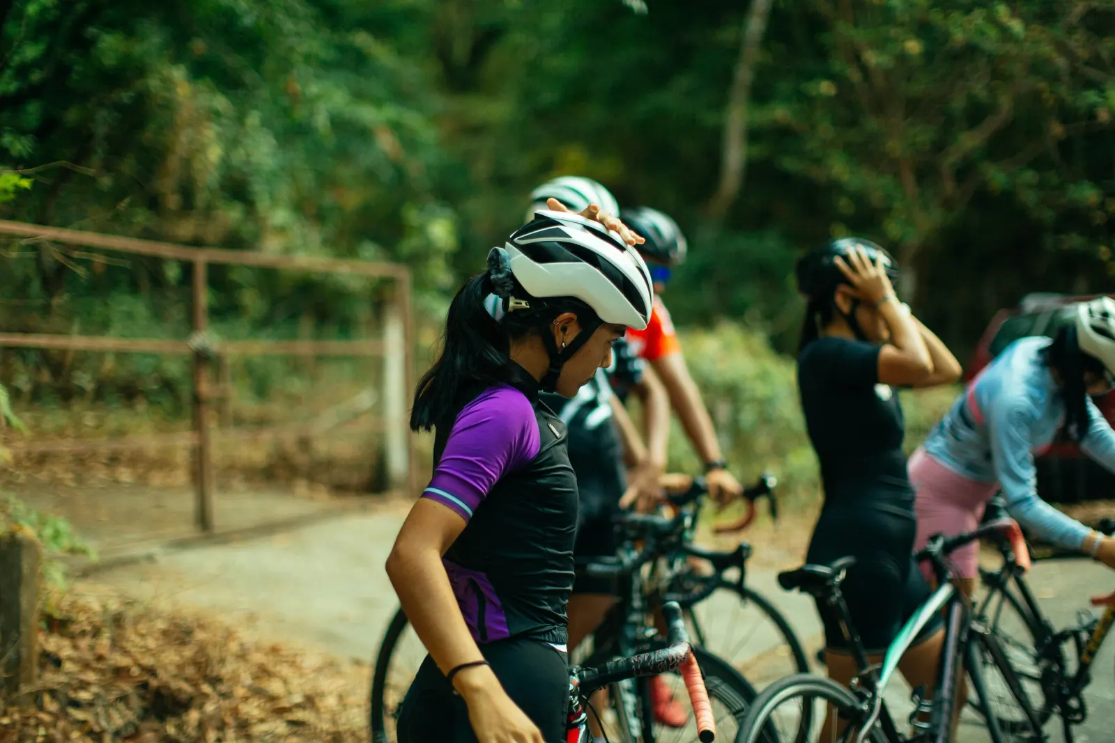 A group of helmeted cyclists gathered with their road bikes on a leafy woodland trail.
