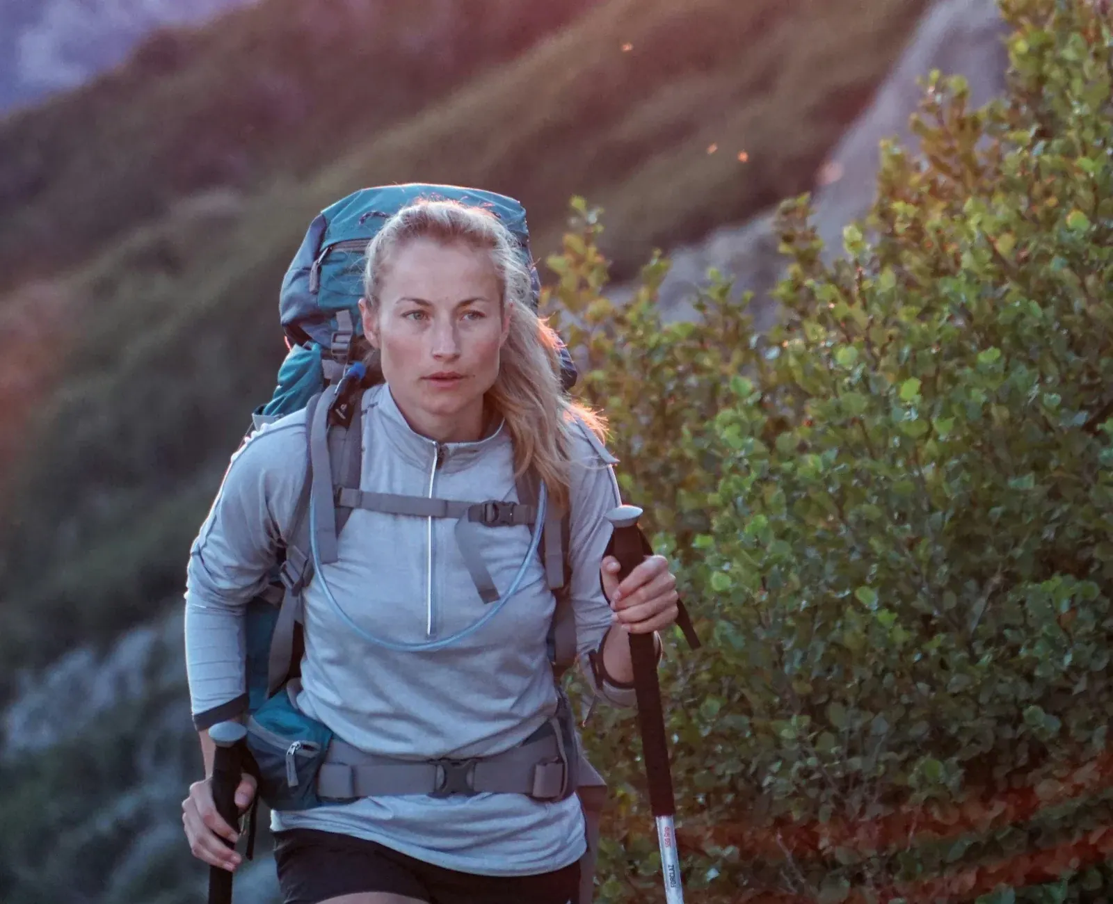 A woman with a backpack and trekking poles hiking along a mountain trail.