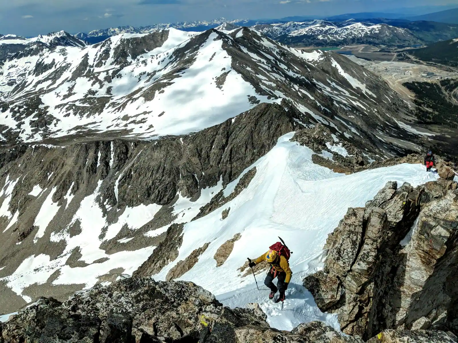 Mountaineers climbing a snow-covered ridge surrounded by rugged alpine peaks.